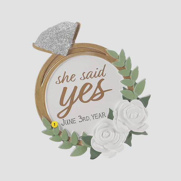 Elegant engagement Christmas ornament featuring gold accents white florals and the phrase she said yes. Personalized with a custom date to commemorate a proposal or engagement moment. A romantic keepsake perfect for celebrating newly engaged couples weddings and meaningful holiday memories.
