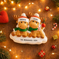 Load image into Gallery viewer, Personalized Christmas ornament with two reindeer wearing hats and scarves on a wooden background with festive decorations.
