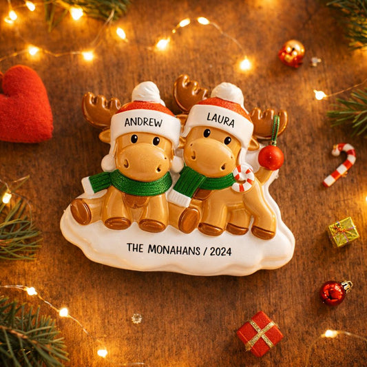 Personalized Christmas ornament with two reindeer wearing hats and scarves on a wooden background with festive decorations.