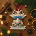 Load image into Gallery viewer, Decorative ornament with goat wearing sunglasses and 'G.O.A.T.' text on a wooden surface with festive items.
