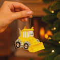 Load image into Gallery viewer, Yellow bulldozer ornament held by a hand with a Christmas tree in the background
