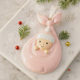 Load image into Gallery viewer, Decorative ornament shaped like a baby in a pink bag with a face, surrounded by Christmas decorations on a marble surface.
