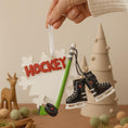 Load image into Gallery viewer, Hockey-themed ornament with skates and stick held by a hand against a neutral background
