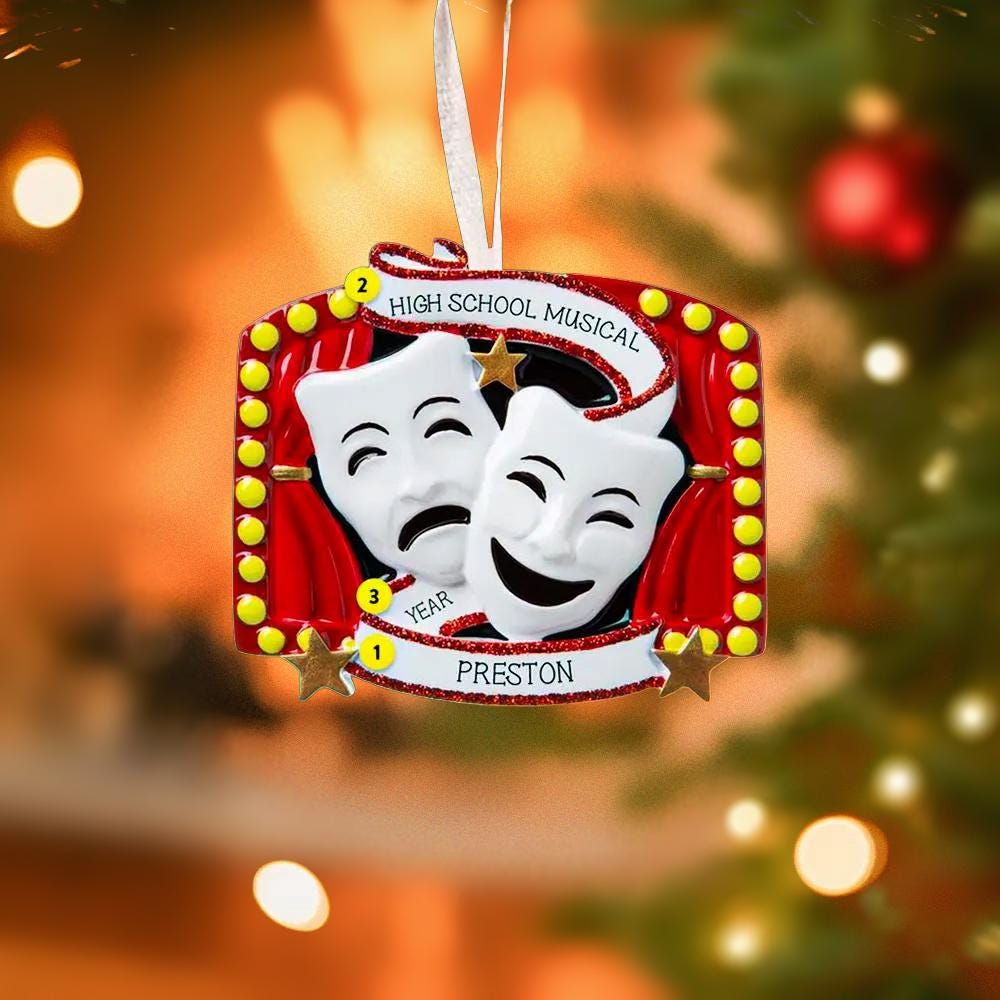 Christmas ornament with theater masks and 'High School Musical' text, hanging on a decorated tree.