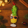 Load image into Gallery viewer, Pineapple ornament with sunglasses on a wooden surface with Christmas decorations.
