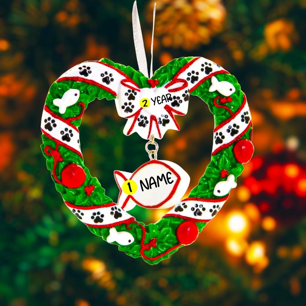 Personalized kitty Christmas ornament designed as a festive heart shaped wreath decorated with cat paw prints fish details and cozy holiday accents. The ornament includes a hanging heart tag that can be personalized with your cat’s name and year. Styled in a warm Christmas setting with soft snow texture and festive colors making it perfect for cat lovers holiday decor cat memorial keepsake and Christmas tree display.