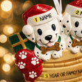 Load image into Gallery viewer, Personalized Christmas dog ornament featuring two adorable dalmatian puppies sitting together on a cozy basket, each wearing a Santa hat and holding a bone. Both puppies can be customized with names, while the front of the basket is personalized with a year or family name. Decorated with festive details like a stocking, gift box, and holiday accents, this ornament has a raised 3D front and smooth finish, making it perfect for dog lovers, couples, families, and Christmas tree decor.

