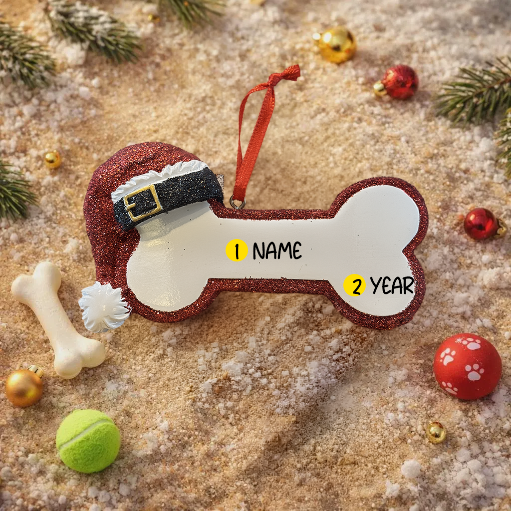 Personalized dog Christmas ornament featuring a bone shaped design with a glitter red Santa hat detail on one end, customizable name area centered on the ornament and customizable year displayed on the opposite side, smooth glossy finish with glitter accents, flat lightweight structure and red hanging ribbon, photographed on a snowy holiday styled background with pine branches, festive Christmas ornaments, dog themed props, and warm seasonal lighting for pet lovers.