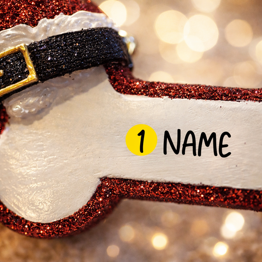 Personalized dog Christmas ornament featuring a bone shaped design with a glitter red Santa hat detail on one end, customizable name area centered on the ornament and customizable year displayed on the opposite side, smooth glossy finish with glitter accents, flat lightweight structure and red hanging ribbon, photographed on a snowy holiday styled background with pine branches, festive Christmas ornaments, dog themed props, and warm seasonal lighting for pet lovers.