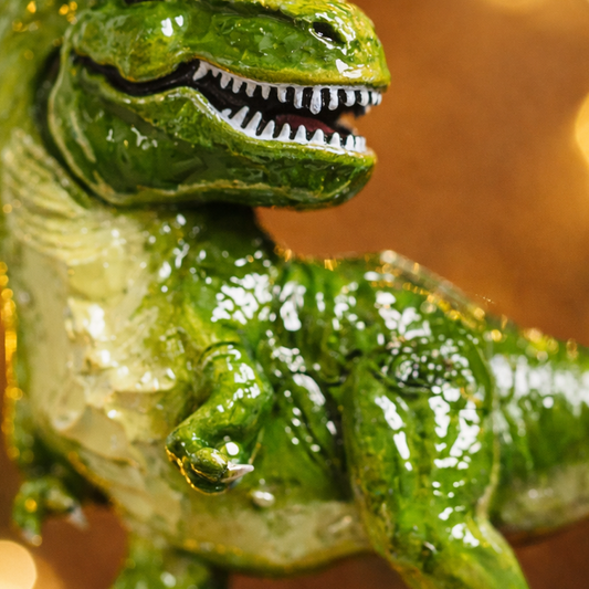 Realistic dinosaur themed Christmas ornament featuring a detailed T-Rex design with vibrant green tones and a playful yet bold appearance. Styled in a warm holiday setting, this ornament is designed to be personalized and makes a fun keepsake for kids who love dinosaurs and adventure themed decorations