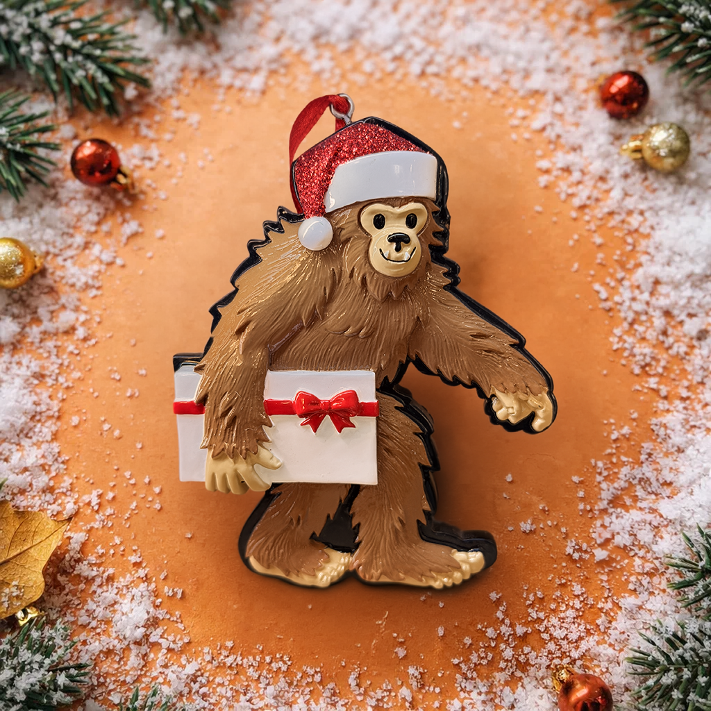 This playful Bigfoot Christmas ornament features a cheerful sasquatch character wearing a Santa hat and holding a gift, finished with a glossy surface that highlights the raised details and festive colors. The design brings a fun and whimsical holiday vibe, making it a standout decoration for Christmas trees, shelves, or seasonal displays, especially for Bigfoot lovers and collectors of unique holiday ornaments.