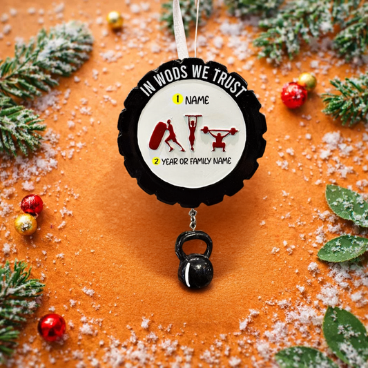 Personalized weightlifting and fitness Christmas ornament featuring a raised 3D front with bold circular design and red strength icons including boxing, gymnastics rings, and weightlifting. The ornament has a textured black outer rim and a flat 2D back for easy hanging. Includes a hanging kettlebell charm for added depth and movement. Hand-added personalization allows a name and year or family name. Photographed on a festive Christmas tree background with warm holiday lights.
