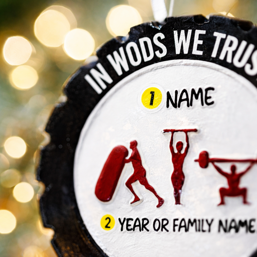 Personalized weightlifting and fitness Christmas ornament featuring a raised 3D front with bold circular design and red strength icons including boxing, gymnastics rings, and weightlifting. The ornament has a textured black outer rim and a flat 2D back for easy hanging. Includes a hanging kettlebell charm for added depth and movement. Hand-added personalization allows a name and year or family name. Photographed on a festive Christmas tree background with warm holiday lights.
