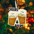 Load image into Gallery viewer, Personalized Cheers and Beers Christmas ornament featuring a raised 3D front with two frothy beer mugs clinking together. The design includes bold “Cheers” and “Beers” lettering, detailed foam texture, and warm amber beer tones. The ornament has a flat 2D back for easy hanging. Hand-added personalization allows two names and a year. Styled on a rustic wooden background with Christmas lights, greenery, and festive decor for a cozy holiday atmosphere.


