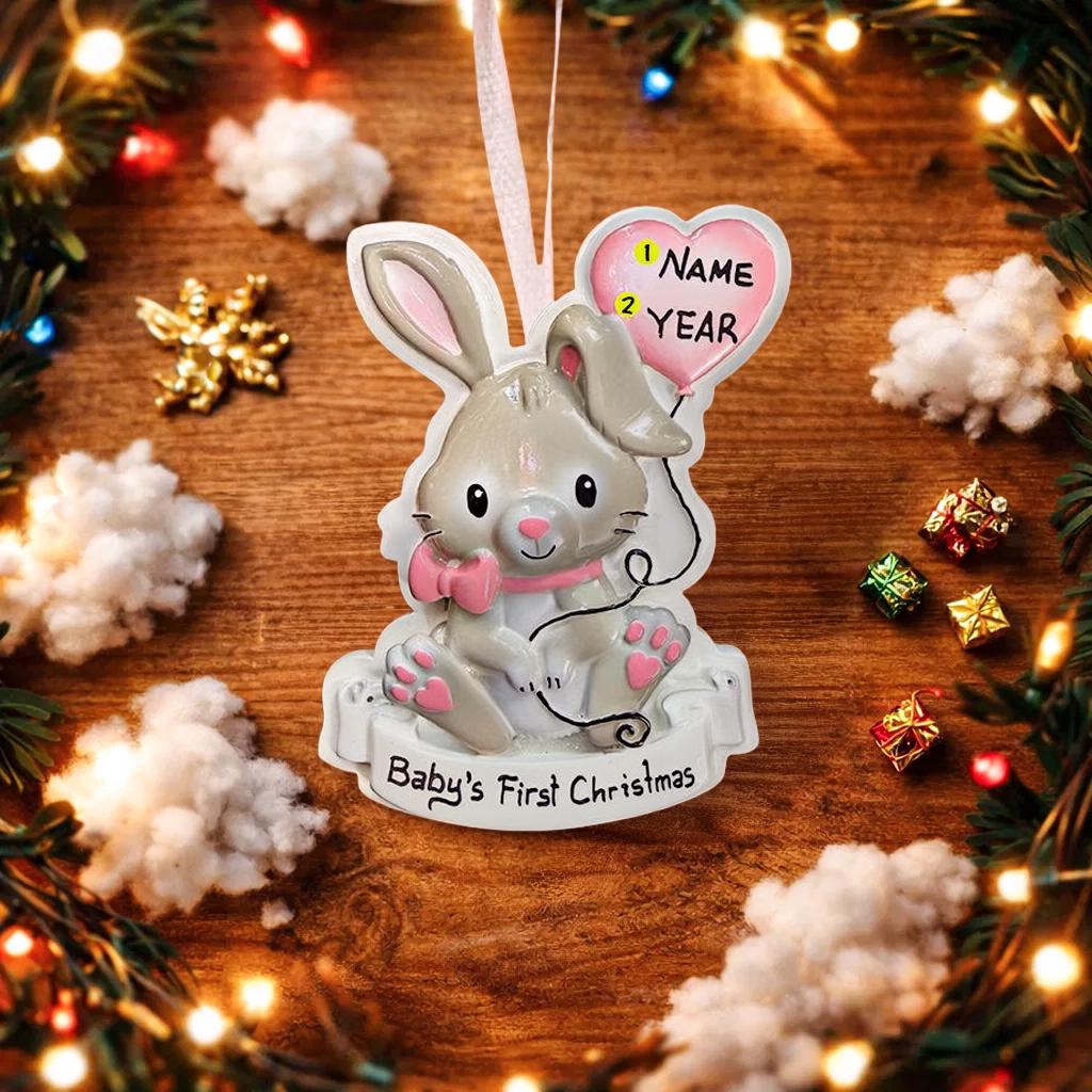 Decorative rabbit ornament for 'Baby's First Christmas' on a wooden surface with festive decorations.