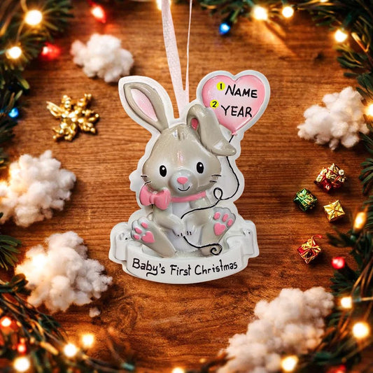 Decorative rabbit ornament for 'Baby's First Christmas' on a wooden surface with festive decorations.