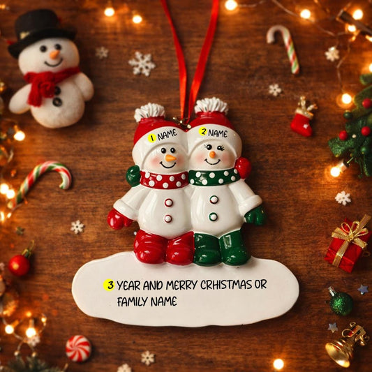 Personalized Christmas ornament with two snowmen on a wooden background with festive decorations.