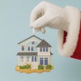Load image into Gallery viewer, Hand holding a house-shaped Christmas ornament against a light blue background
