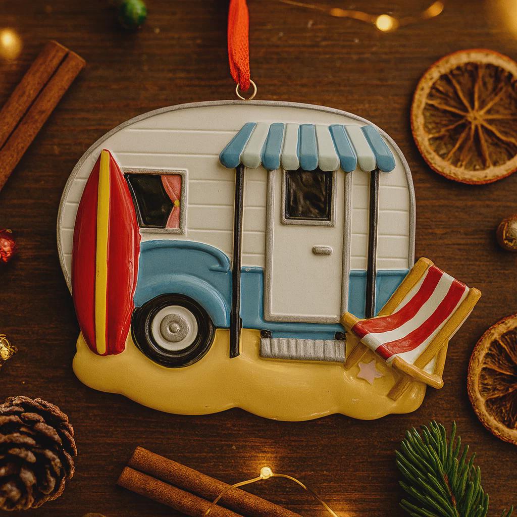 Decorative ornament of a camper with a surfboard and beach chair on a wooden surface.