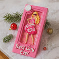 Load image into Gallery viewer, A vibrant pink fashion doll ornament with a retro camera-frame look and floral dress, perfect for holiday trees. Features bright colors, playful style, and a customizable area for adding a name or short text. Designed as a fun keepsake for kids and collectors who love bold, glamorous ornaments. Ideal for Christmas décor, stocking stuffers, and memorable seasonal gifting.
