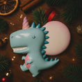 Load image into Gallery viewer, Decorative ornament shaped like a dragon with a unicorn horn on a wooden surface with Christmas decorations.
