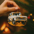 Load image into Gallery viewer, Hand holding a Christmas ornament shaped like a vintage SUV with a snowy design against a blurred festive background.
