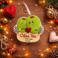 Load image into Gallery viewer, Decorative ornament with two smiling green olives holding a heart, surrounded by Christmas decorations on a wooden surface.
