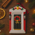 Load image into Gallery viewer, Decorative Christmas ornament resembling a door with a wreath, surrounded by festive items on a wooden surface.
