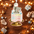 Load image into Gallery viewer, Personalized gender reveal Christmas ornament for baby girl featuring a pastel cake design with a cute elephant topper and its a gender message, soft pink and blue tones with layered cake details and glossy finish, styled as a sweet holiday keepsake for expecting parents, baby announcement and first Christmas memories, displayed on a warm wooden background with cozy Christmas lights, baby shoes and festive decor creating a joyful and heartwarming celebration scene
