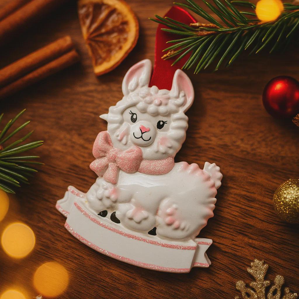 A glossy resin baby girl llama ornament features a white smiling llama with soft pink accents, raised textured fur details, pink bow and scarf elements, glitter highlights, and a smooth painted cartoon style finish, styled with warm holiday lights and nursery themed props, handwritten personalization showing the baby name on the front banner and the year placed on the llama body, designed as a mostly 2D ornament with raised 3D details on the front only.