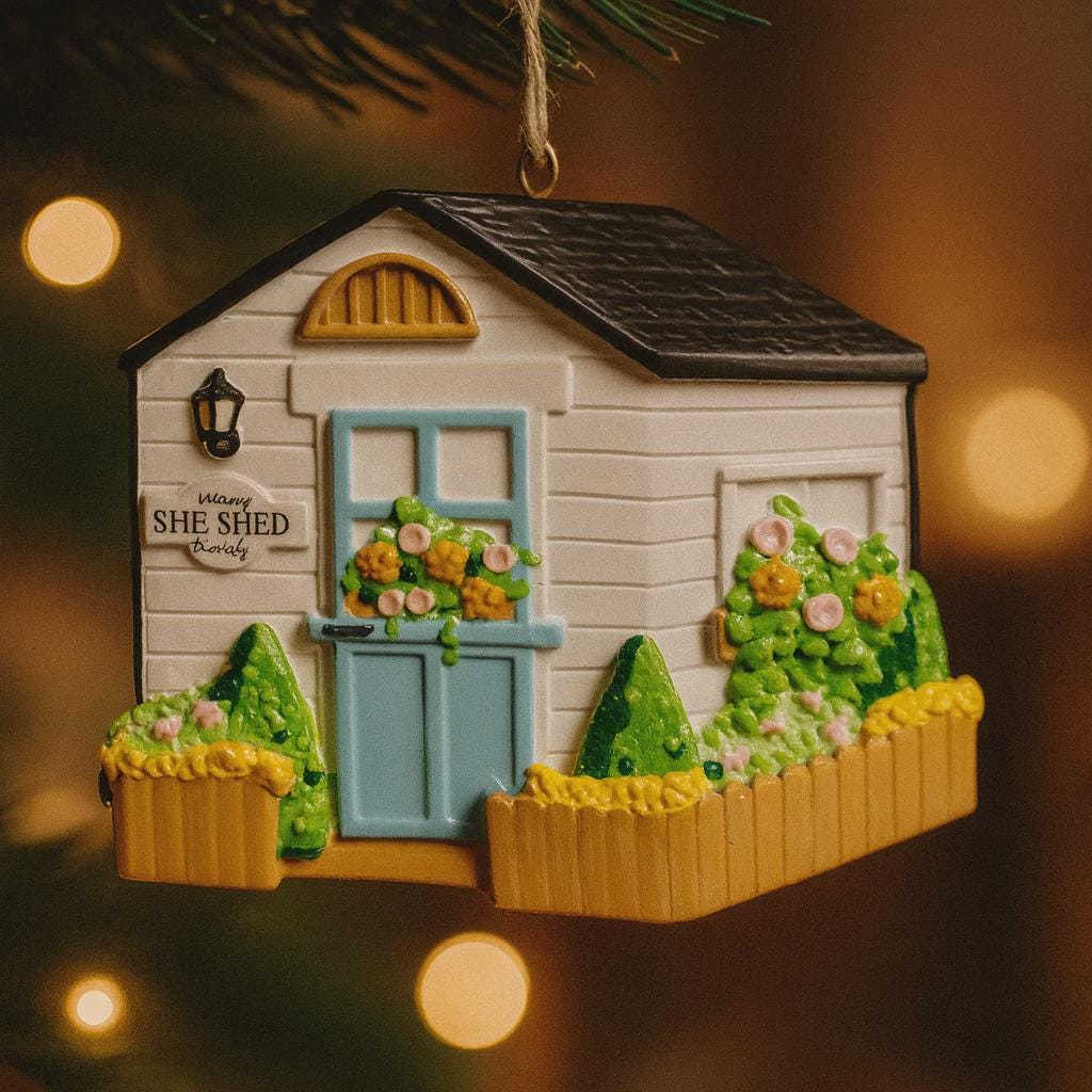 Decorative ornament of a small house with 'SHE SHED' sign on a blurred light background