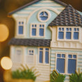 Load image into Gallery viewer, Decorative cookie in the shape of a house with a clock on the roof, against a blurred background.
