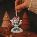 Load image into Gallery viewer, Decorative Christmas ornament of a squirrel holding a bag and gift, held by a hand with a festive background.
