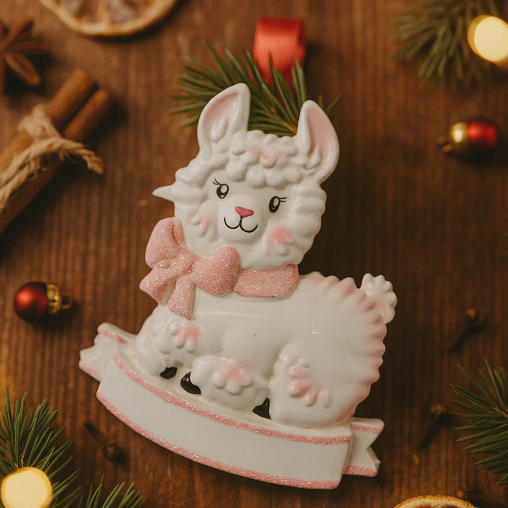 A glossy resin baby girl llama ornament features a white smiling llama with soft pink accents, raised textured fur details, pink bow and scarf elements, glitter highlights, and a smooth painted cartoon style finish, styled with warm holiday lights and nursery themed props, handwritten personalization showing the baby name on the front banner and the year placed on the llama body, designed as a mostly 2D ornament with raised 3D details on the front only.