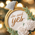 Load image into Gallery viewer, Elegant engagement Christmas ornament featuring gold accents white florals and the phrase she said yes. Personalized with a custom date to commemorate a proposal or engagement moment. A romantic keepsake perfect for celebrating newly engaged couples weddings and meaningful holiday memories.
