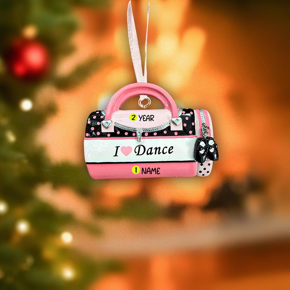 Decorative ornament shaped like a pink ballet slipper with 'I ❤️ Dance' text, on a blurred Christmas tree background.