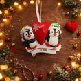 Load image into Gallery viewer, Personalized Christmas ornament with two penguins and a heart on a wooden surface with festive decorations.
