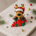 Load image into Gallery viewer, Christmas-themed figurine of a reindeer in a Santa hat with lights on a decorative surface.
