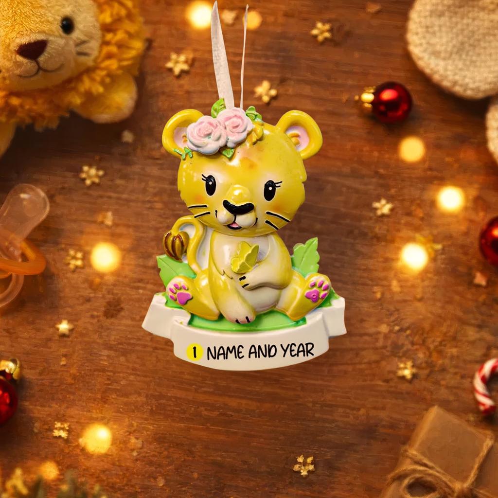Personalized baby lion Christmas ornament featuring a sweet yellow lion cub wearing a floral crown and holding a small leaf. The bottom banner can be customized with name and year, creating a unique keepsake for a newborn or toddler. Designed in warm yellow and soft pastel tones, this resin baby Christmas ornament is perfect for celebrating Baby’s First Christmas or adding a personalized jungle themed touch to your holiday tree.