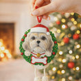 Load image into Gallery viewer, Dog Christmas ornament with a wreath and Santa hat, held by a hand against a festive background.
