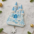 Load image into Gallery viewer, Decorative cookie shaped like a castle with blue towers and snowflakes on a white background.
