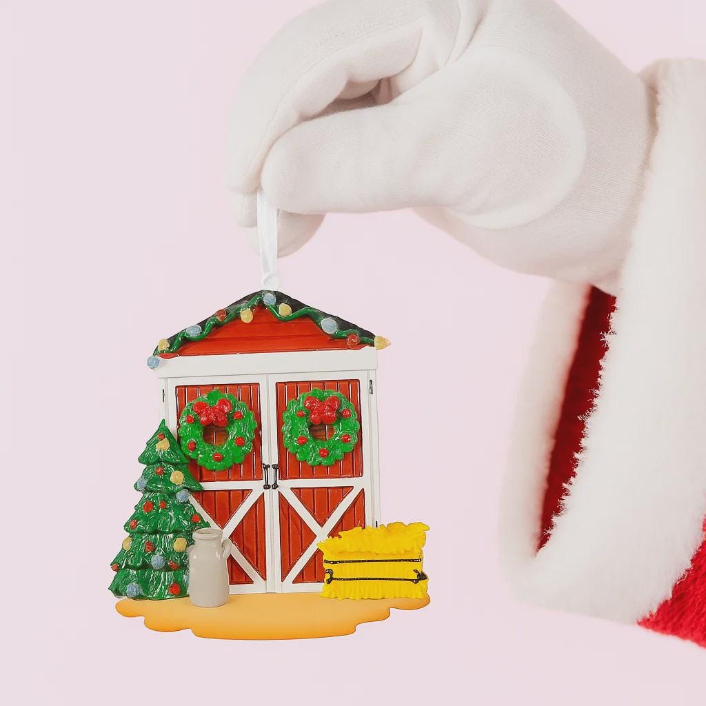 Decorative Christmas ornament shaped like a barn with festive elements held by a gloved hand.
