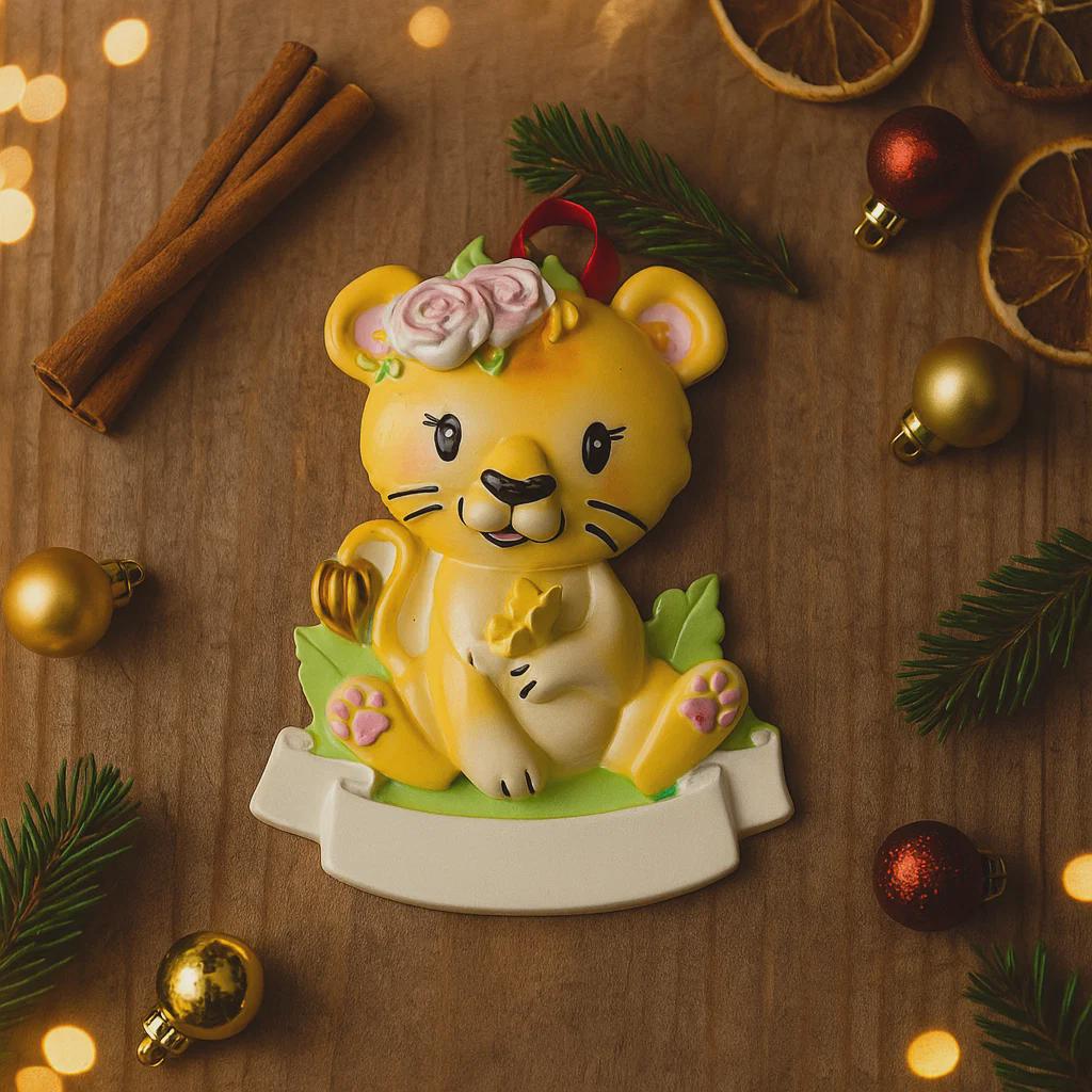 Personalized baby lion Christmas ornament featuring a sweet yellow lion cub wearing a floral crown and holding a small leaf. The bottom banner can be customized with name and year, creating a unique keepsake for a newborn or toddler. Designed in warm yellow and soft pastel tones, this resin baby Christmas ornament is perfect for celebrating Baby’s First Christmas or adding a personalized jungle themed touch to your holiday tree.