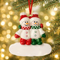 Load image into Gallery viewer, Two snowman ornaments in red and green attire hanging from a tree branch with a festive background.
