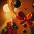 Load image into Gallery viewer, Close-up of a gingerbread man-shaped cookie ornament with a blurred light in the background
