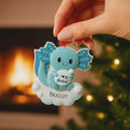 Load image into Gallery viewer, Decorative ornament with a blue creature design, held by a hand against a festive background.

