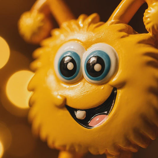 Close-up of a yellow plush toy with large blue eyes and a blurred golden background