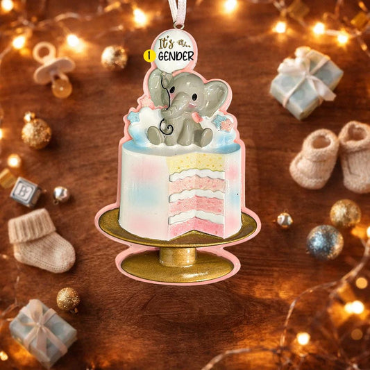 Personalized gender reveal Christmas ornament for baby girl featuring a pastel cake design with a cute elephant topper and its a gender message, soft pink and blue tones with layered cake details and glossy finish, styled as a sweet holiday keepsake for expecting parents, baby announcement and first Christmas memories, displayed on a warm wooden background with cozy Christmas lights, baby shoes and festive decor creating a joyful and heartwarming celebration scene