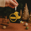 Load image into Gallery viewer, USB drive shaped like a tape measure with Christmas decorations in the background
