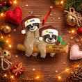 Load image into Gallery viewer, Two sloth ornaments on a branch with Christmas decorations on a wooden surface.
